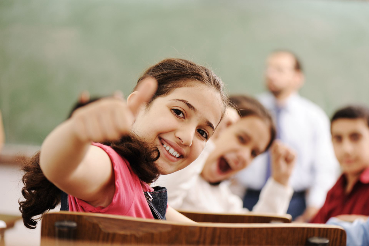 Happy children smiling and laughing in the classroom, showing thumb up, successful pupils and teacher